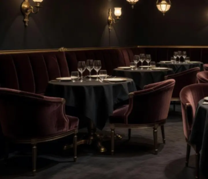 Salle à manger intimiste avec tables nappées, banquettes de velours grenat et appliques en laiton.
